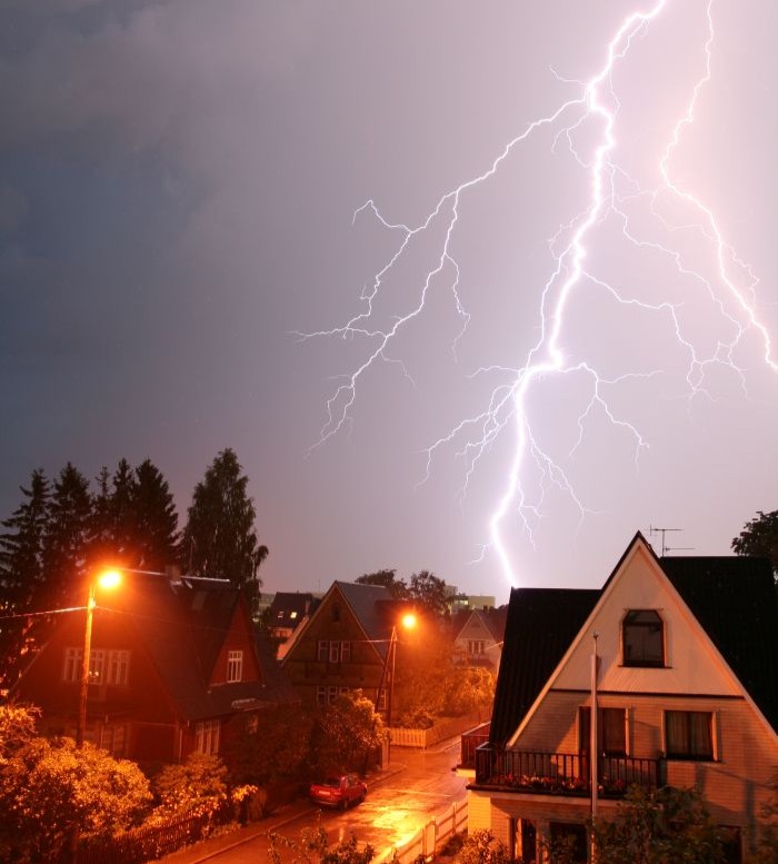 Lightning striking near a residential neighborhood during a severe thunderstorm, illustrating a potential source of power outages.